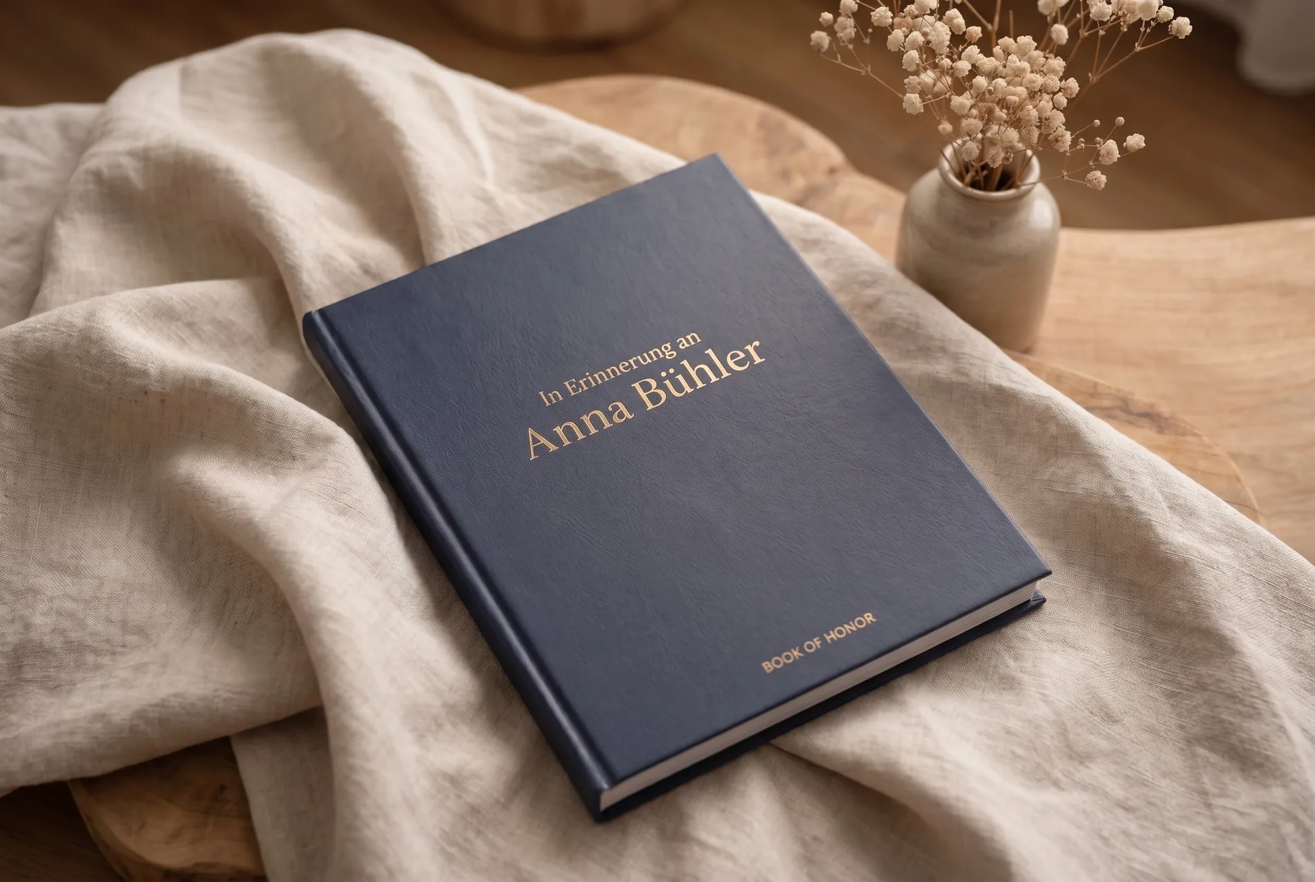 A printed memorial book in deep navy on light linen, with dried flowers beside it.
